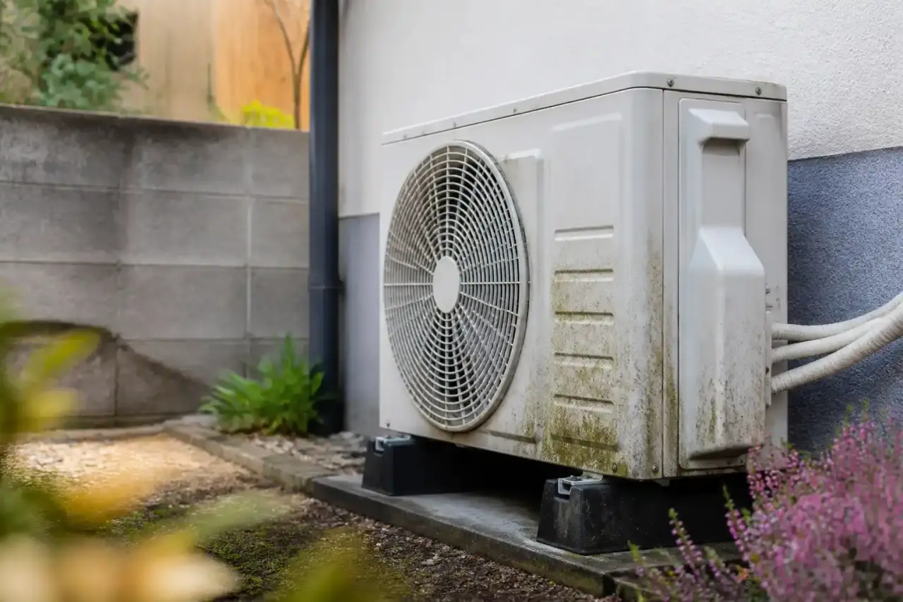 Unité extérieure de pompe à chaleur installée près d'une maison moderne avec végétation